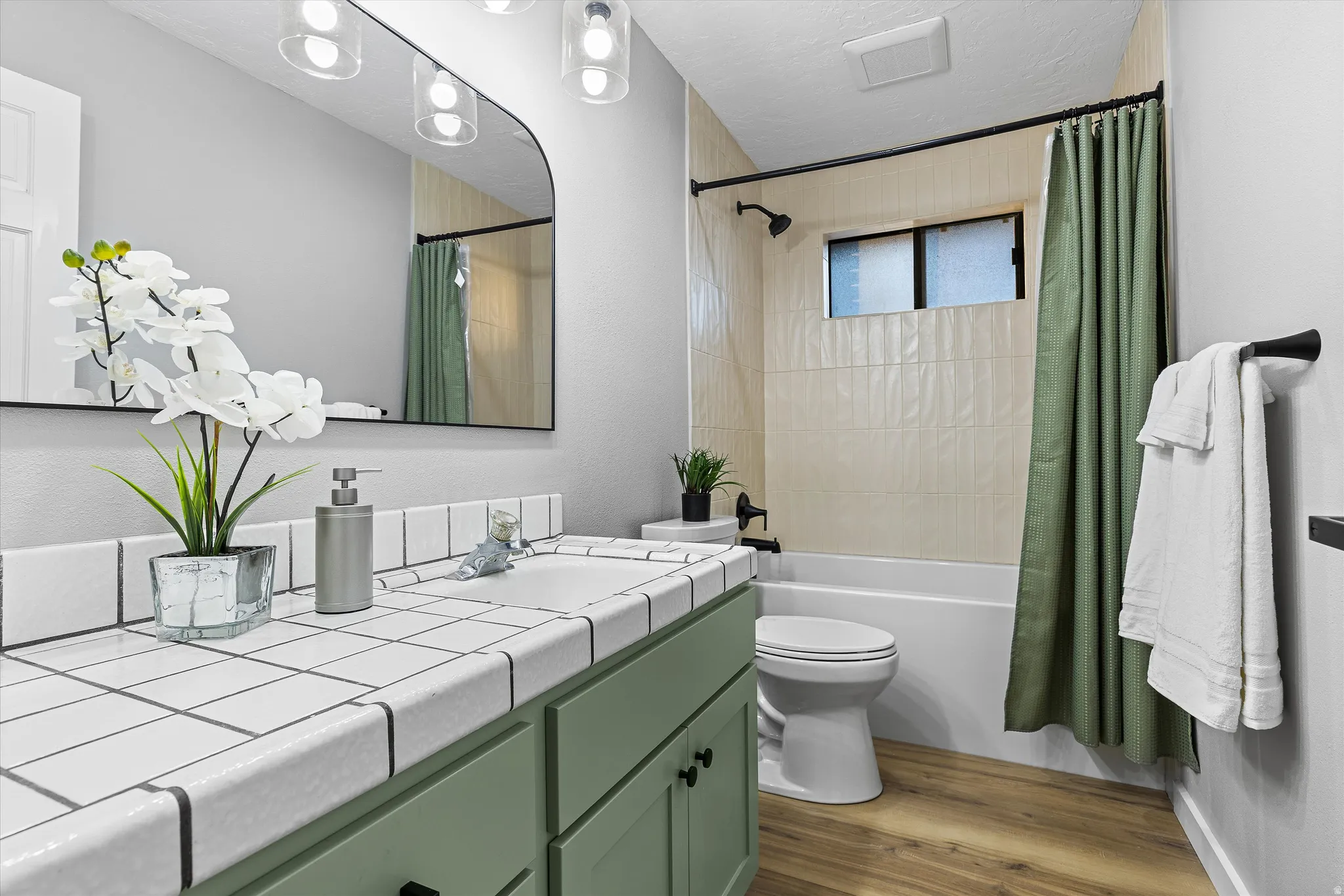 Updated Main-Floor Bathroom. Bathroom vanity with white square tile countertop, sage green cabinetry, a black-framed arched mirror, and a three-light fixture