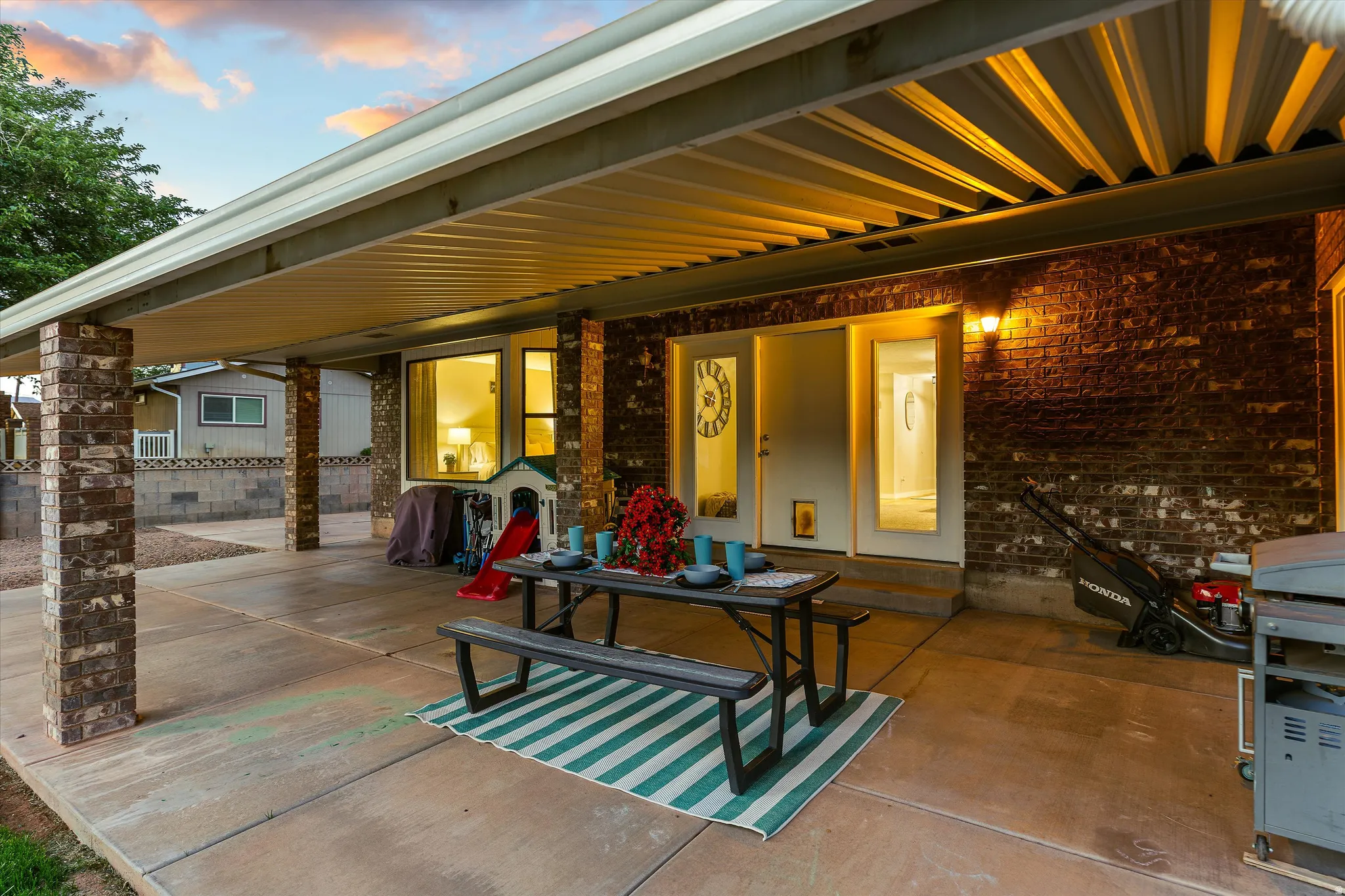 Patio Glowing at Twilight. Expansive covered patio featuring a corrugated metal ceiling and brick-clad support columns