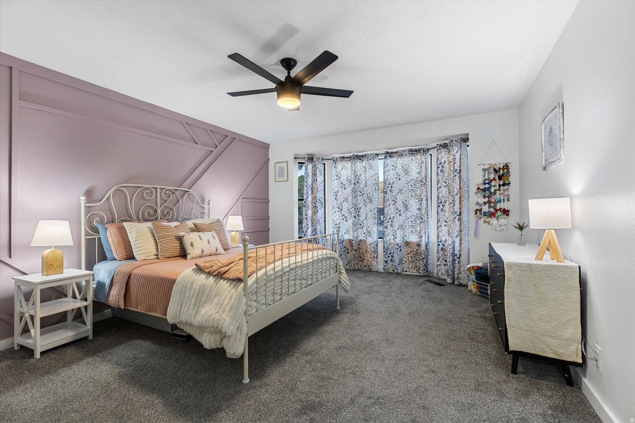 Main-Floor Secondary Bedroom. Bedroom featuring a decorative accent wall, ceiling fan with integrated lighting, and a prominent bay window
