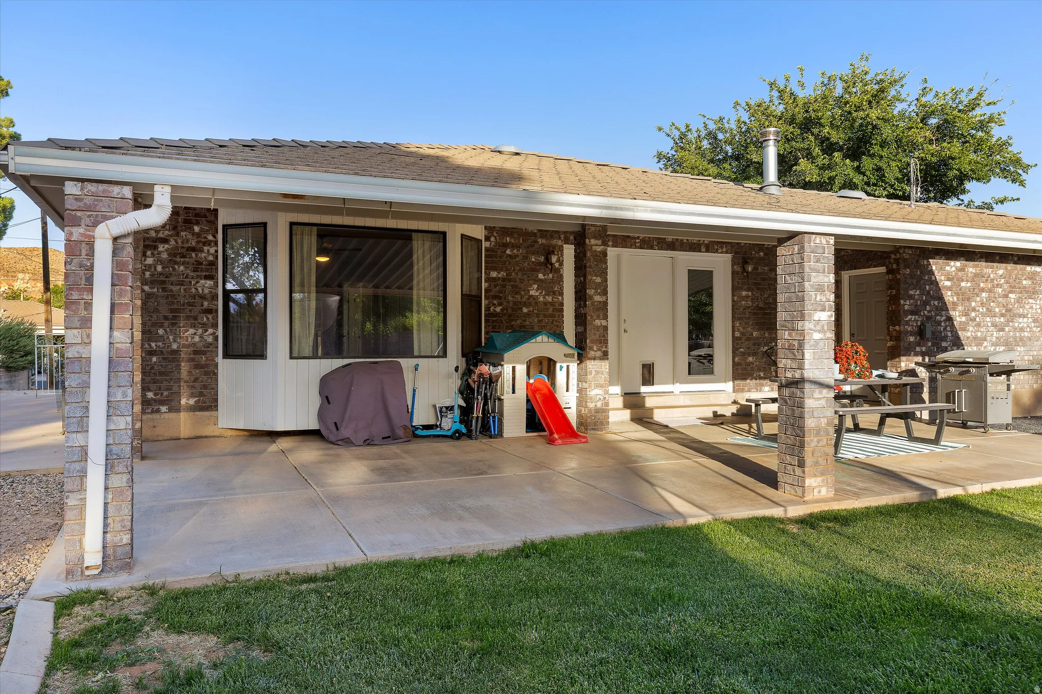Daytime View of the Back Patio. Expansive covered patio featuring brick columns, a light-colored roofline, and a multi-pane bay window