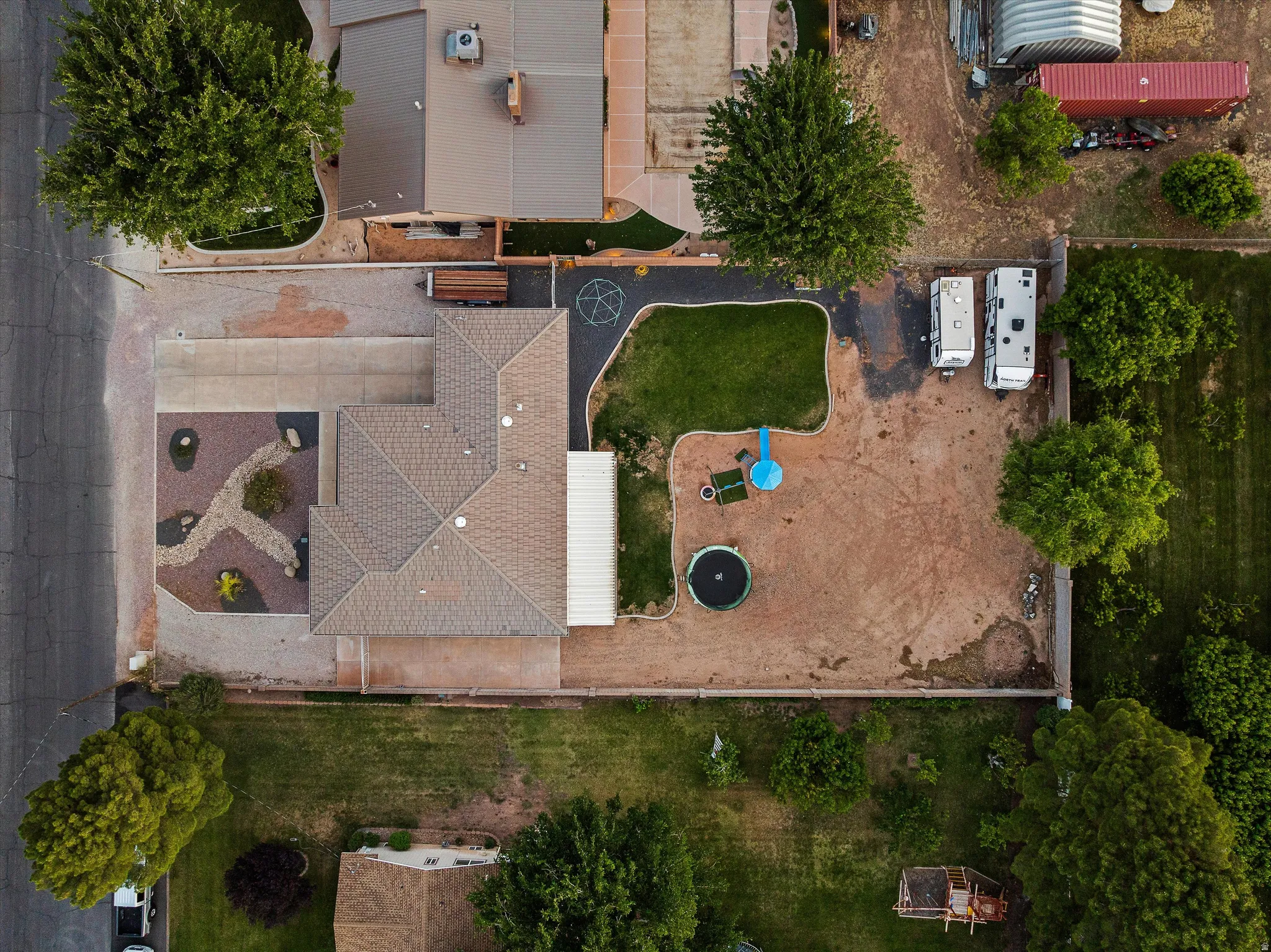 Overhead View of the Property. Property featuring a gabled roof, an expansive paved patio, and a landscaped rock garden