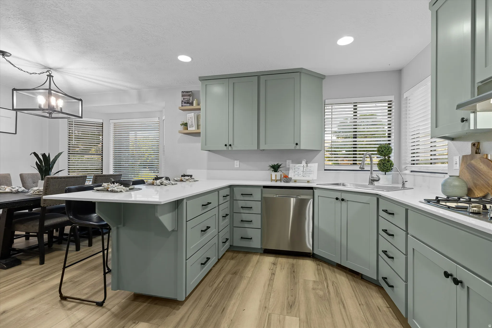 Modern Kitchen with Quartz Counters. Contemporary kitchen featuring light green cabinetry, white countertops, stainless steel appliances, wood-finish flooring, and a breakfast bar