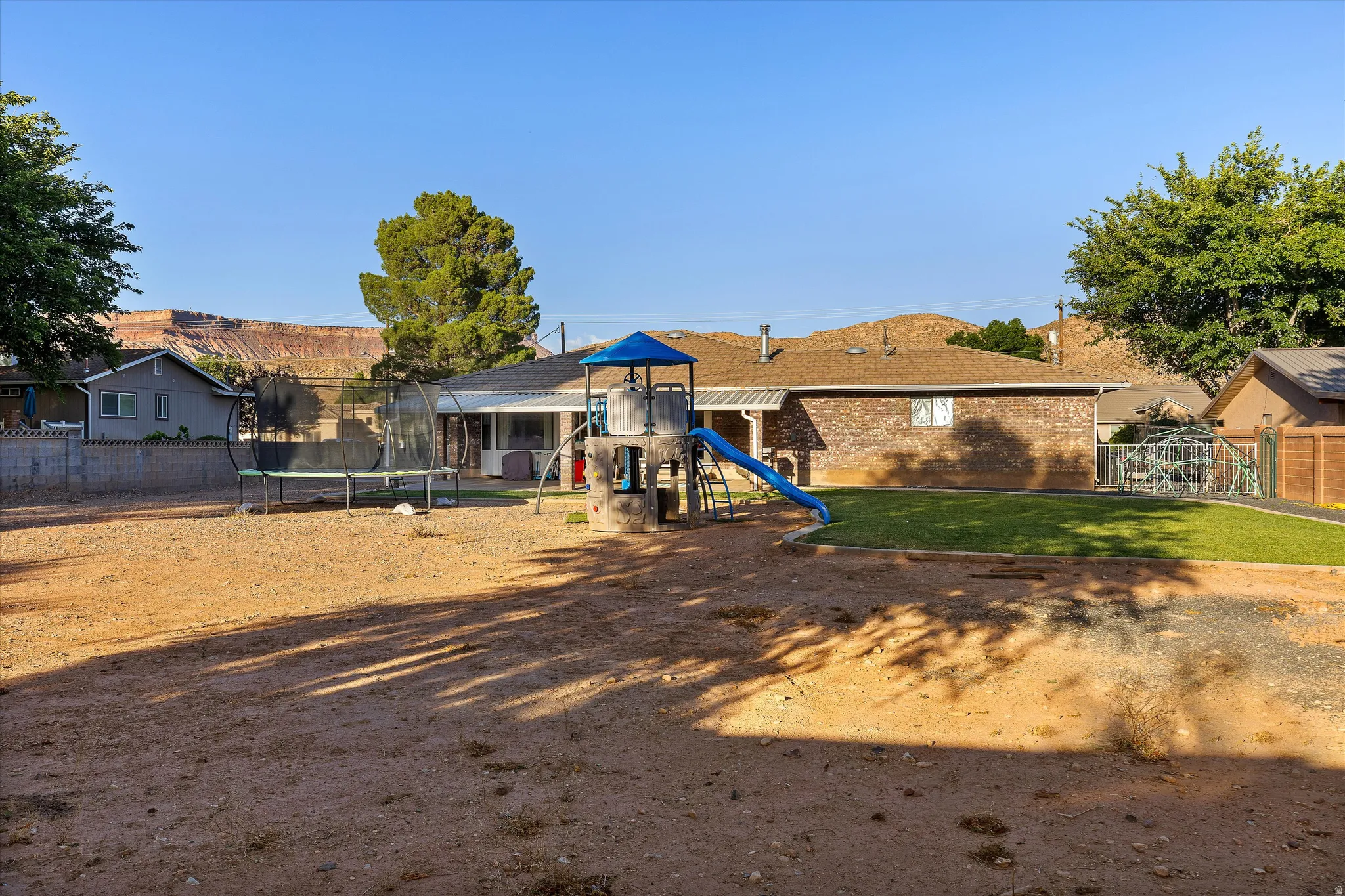 Open Yard Space — A Blank Canvas. Spacious backyard featuring a large unlandscaped area, a manicured lawn section, and a brick exterior dwelling with a brown shingle roof