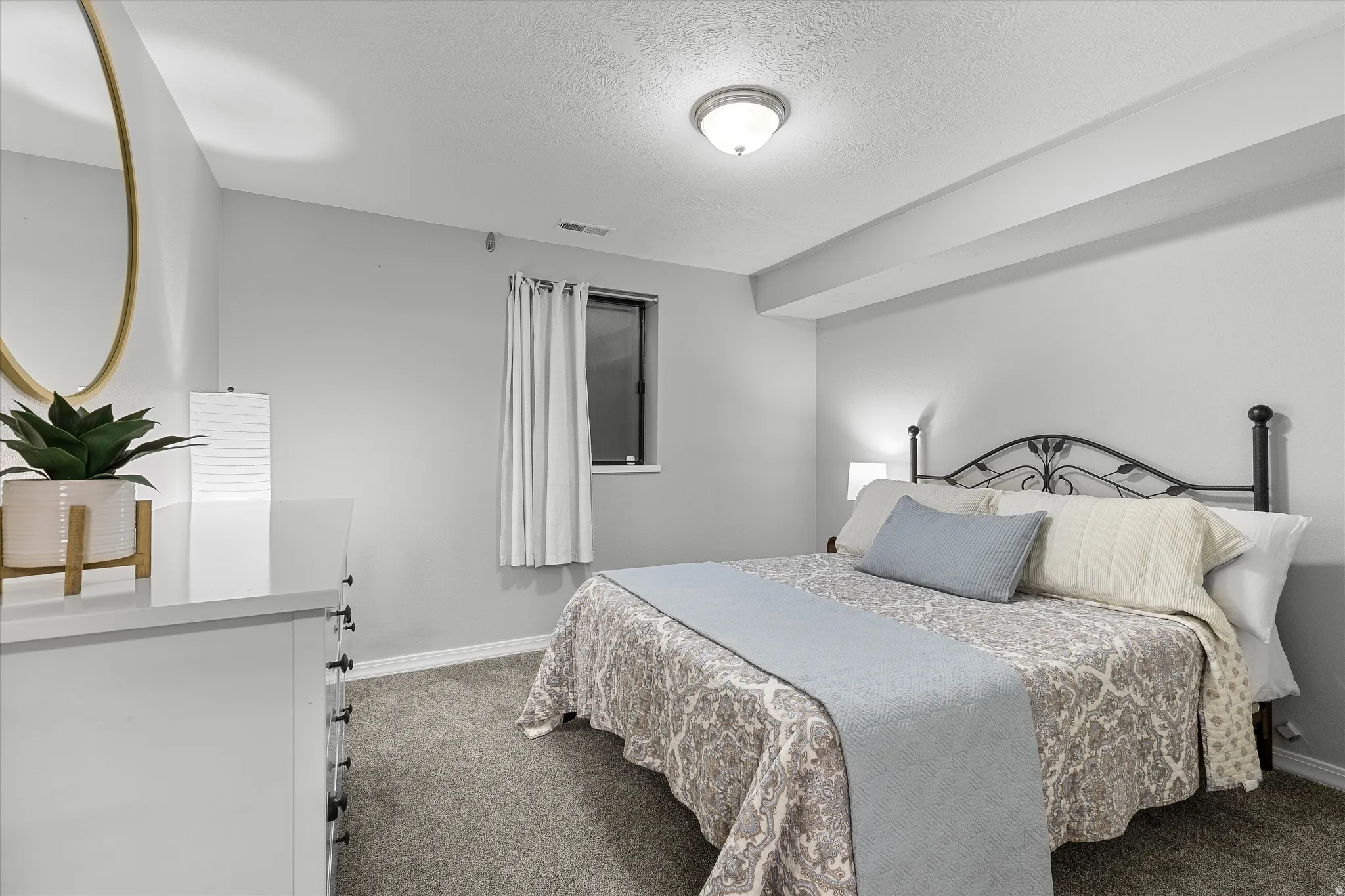 Basement Bedroom. Carpeted bedroom featuring a window with privacy blinds, a flush-mount ceiling light fixture, and a built-in recessed ceiling section