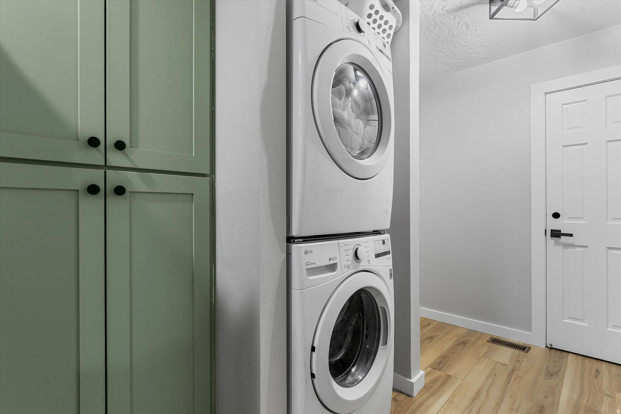 Built-In Stackable Laundry. Laundry area featuring a stacked washer and dryer, light green shaker-style cabinetry with black hardware, wood-finish flooring, and a contemporary ceiling light fixture