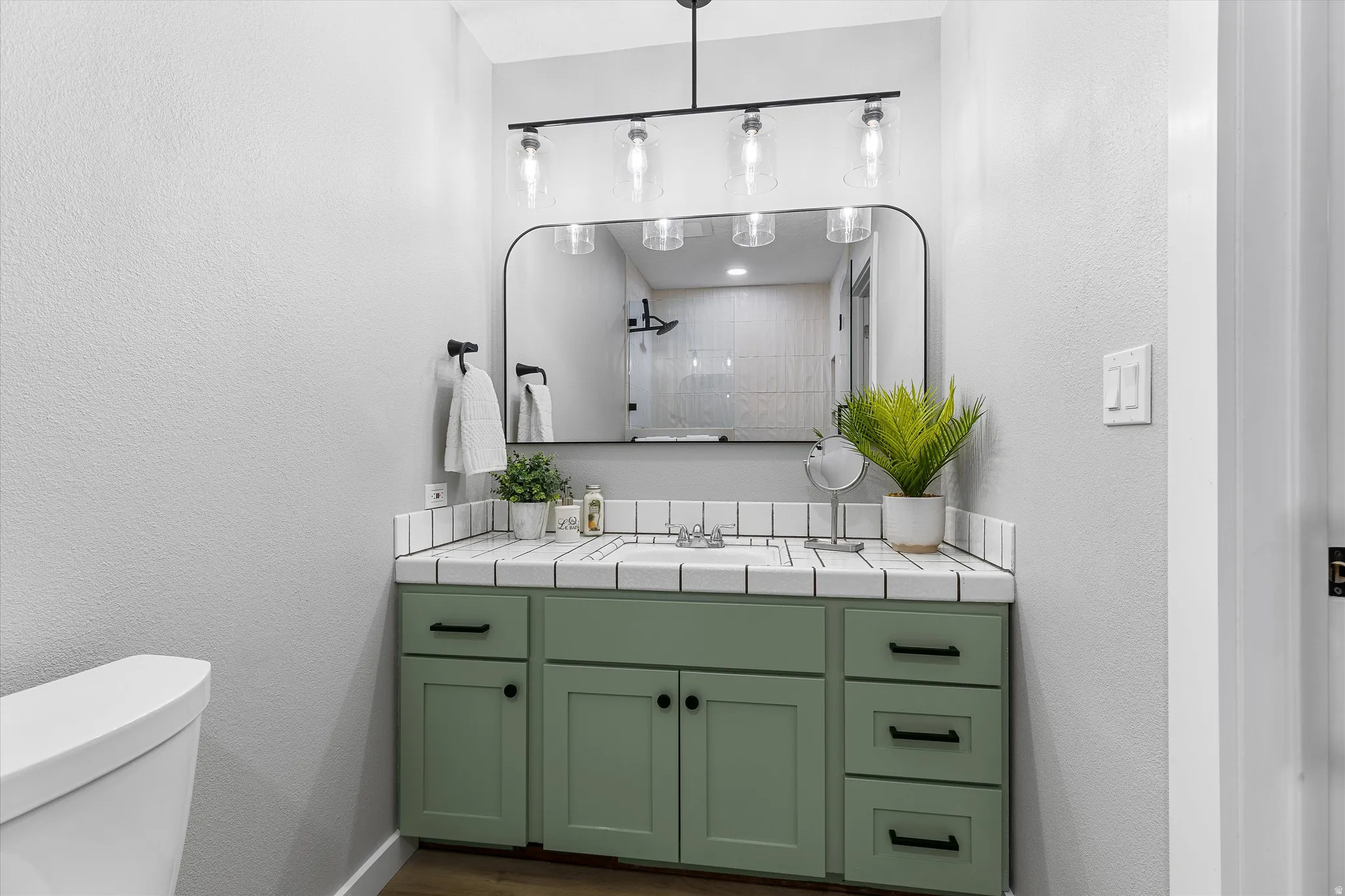 Updated Primary Bath with Sage Vanity. Bathroom vanity featuring a sage green cabinet with black hardware, a white tile countertop, and a contemporary framed mirror