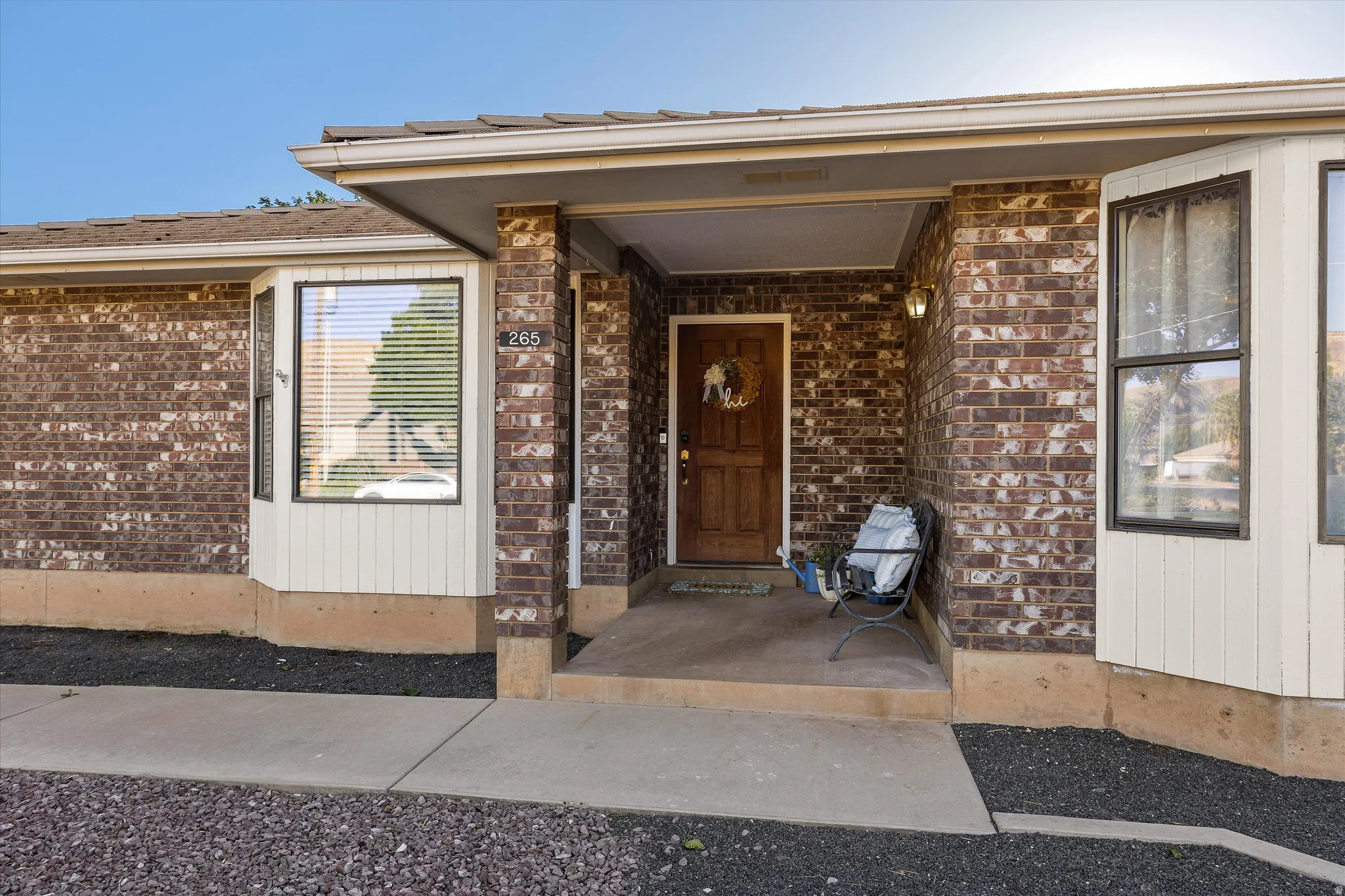 Inviting Front Entry. Brick exterior featuring a covered entry, an inset wood-panel front door, and flanking bay windows with vertical siding accents