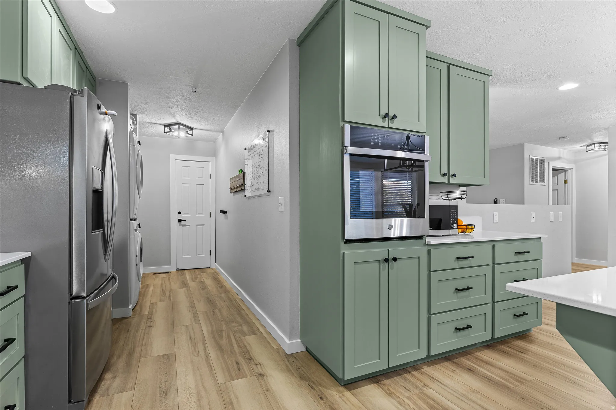 Kitchen Hallway with Pantry Access. Kitchen featuring contemporary sage cabinetry, light-toned wood-finish flooring, a stainless steel built-in oven, and white countertops