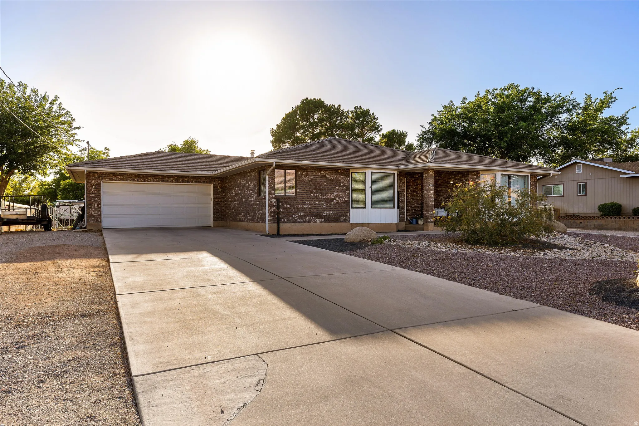 Daytime Driveway & Garage View. Brick exterior residence featuring a two-car garage with a concrete driveway, a prominent bay window, and low-maintenance xeriscape landscaping