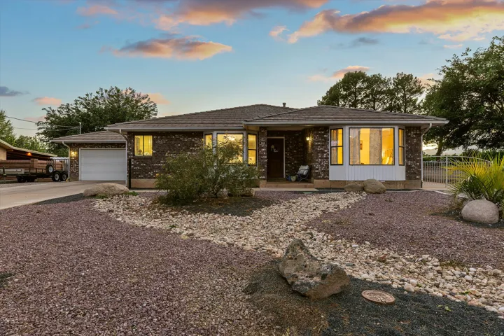 Welcoming Curb Appeal in La Verkin. Brick exterior featuring a bay window, an attached garage, a covered entry, and a gravel and rock landscape