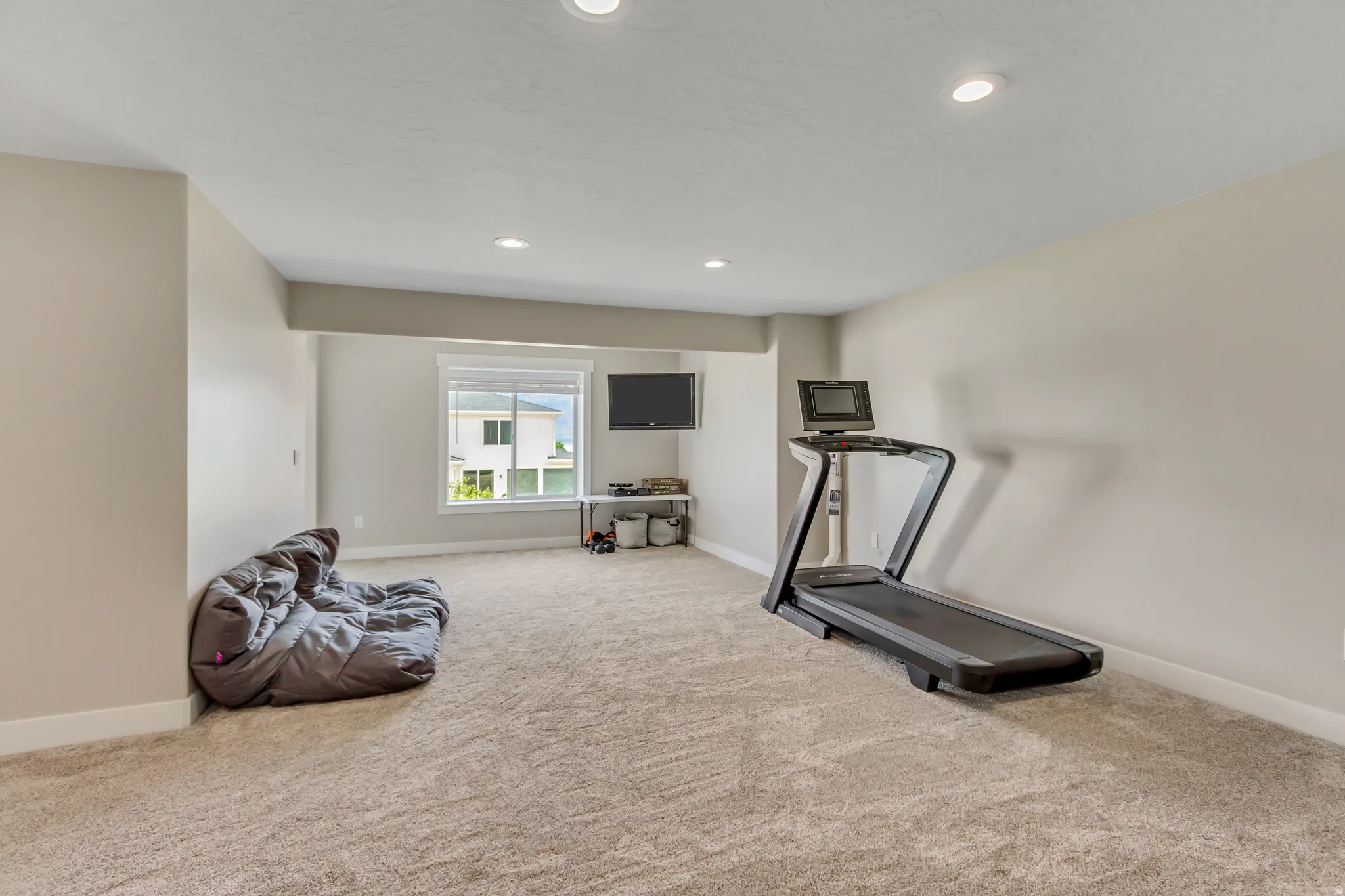 Spacious room featuring neutral carpeting, recessed lighting, and a large window with white blinds