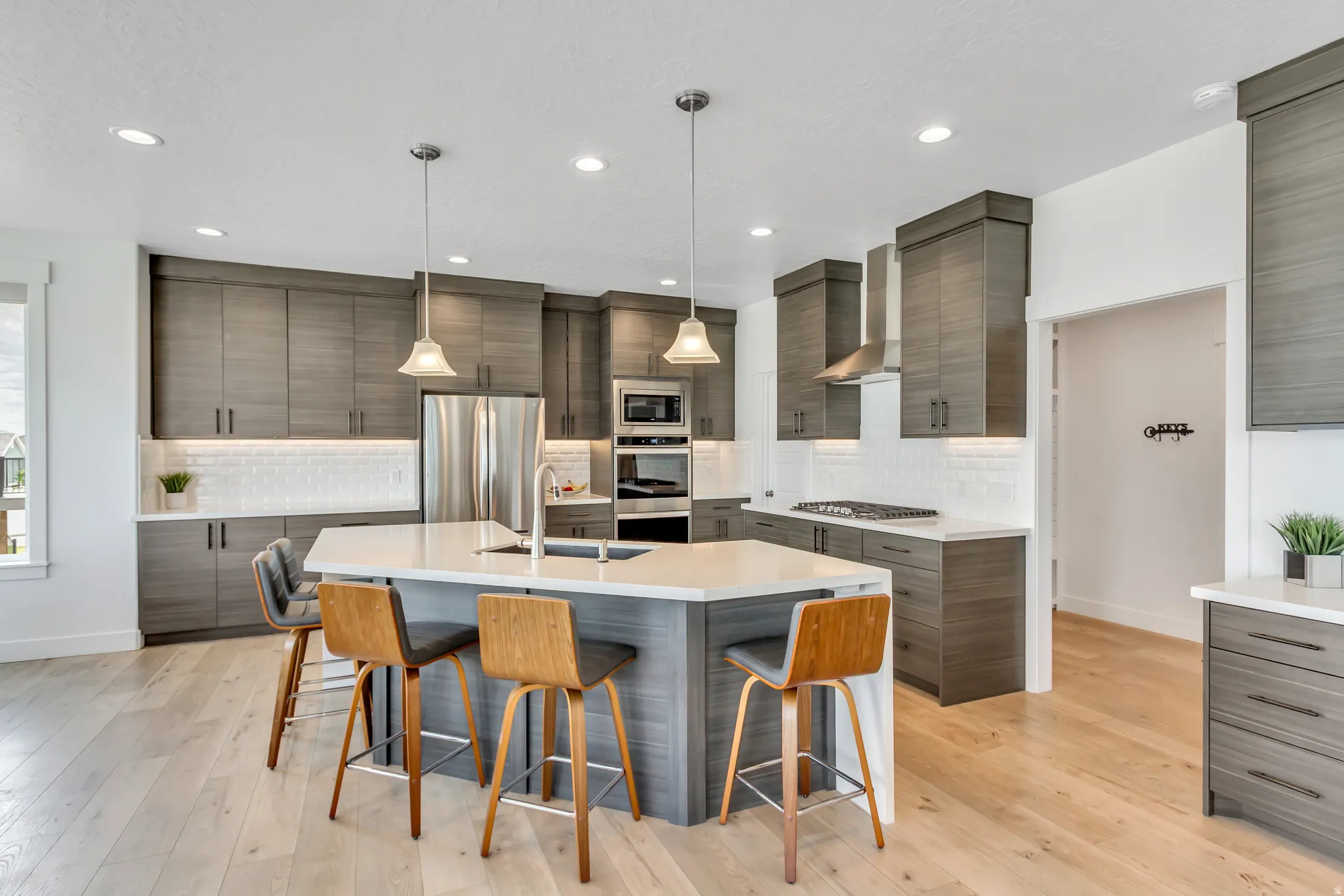 Open-concept kitchen featuring an angular island with a sink and waterfall quartz countertops, stainless steel appliances and hood.