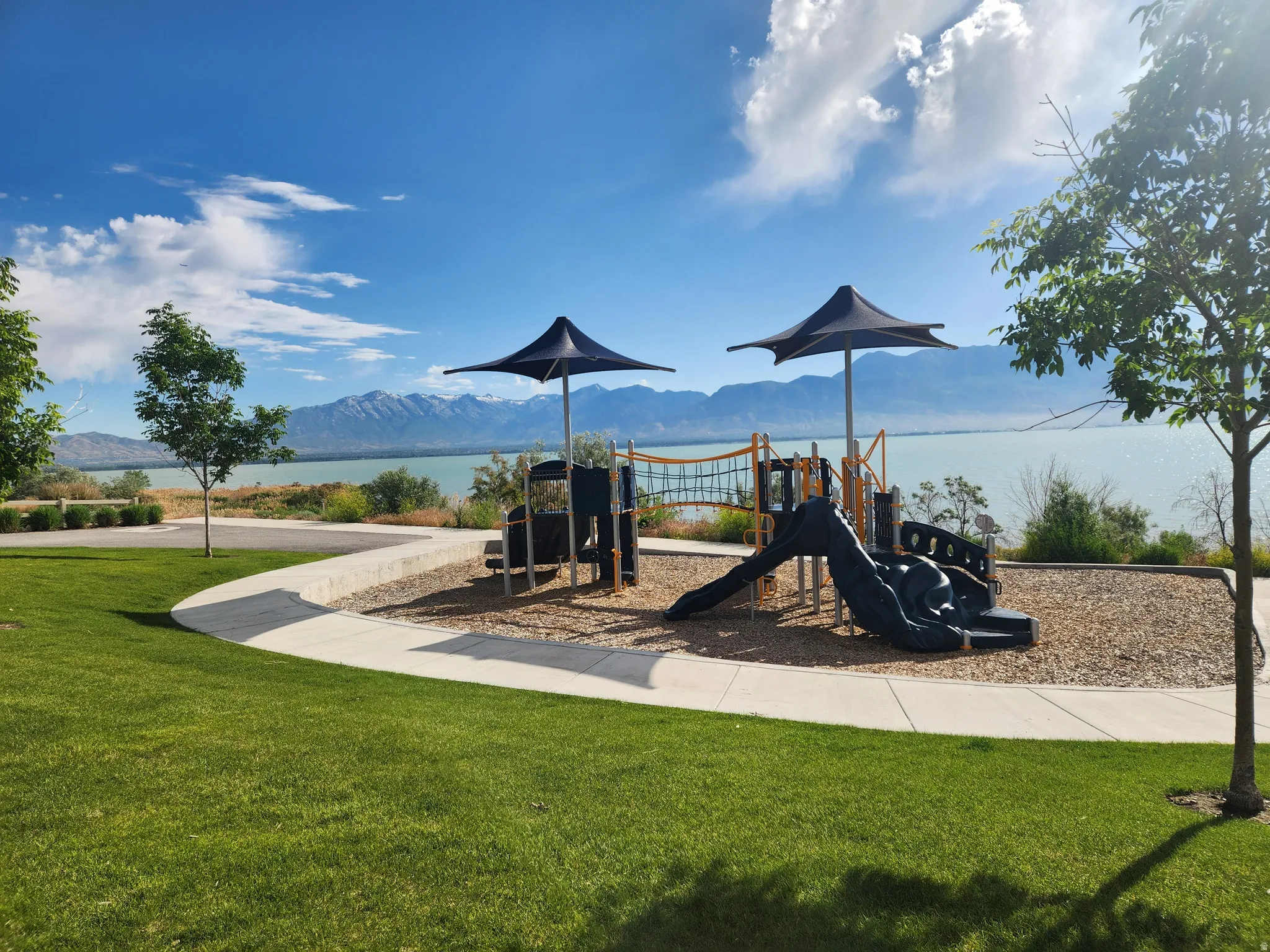 Community playground  is one block from home, featuring shade structures, a climbing net, and a slide, all set against a tranquil lake and mountain backdrop.