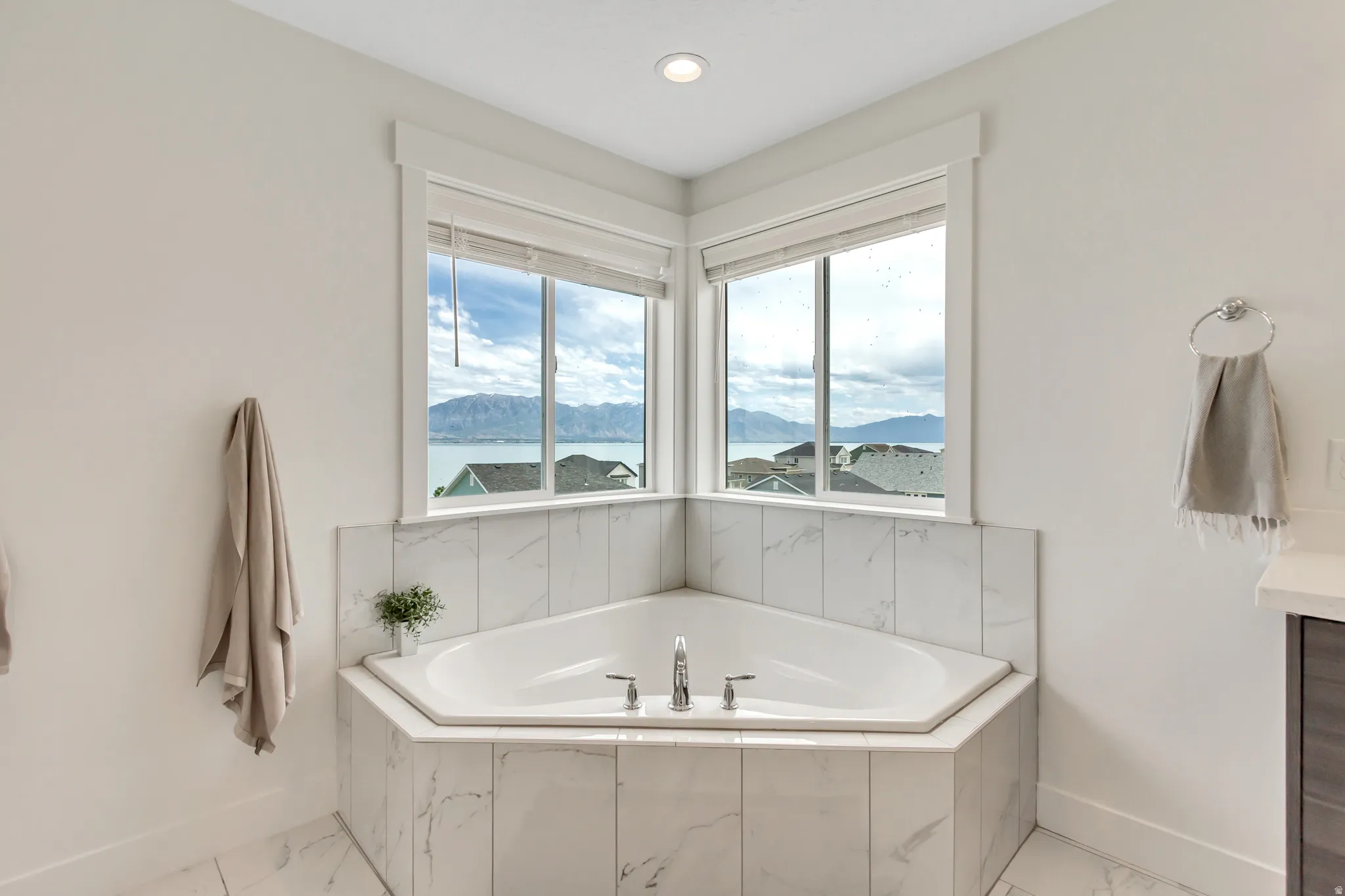 Corner soaking tub with beautiful views and marble-look tile surround and deck