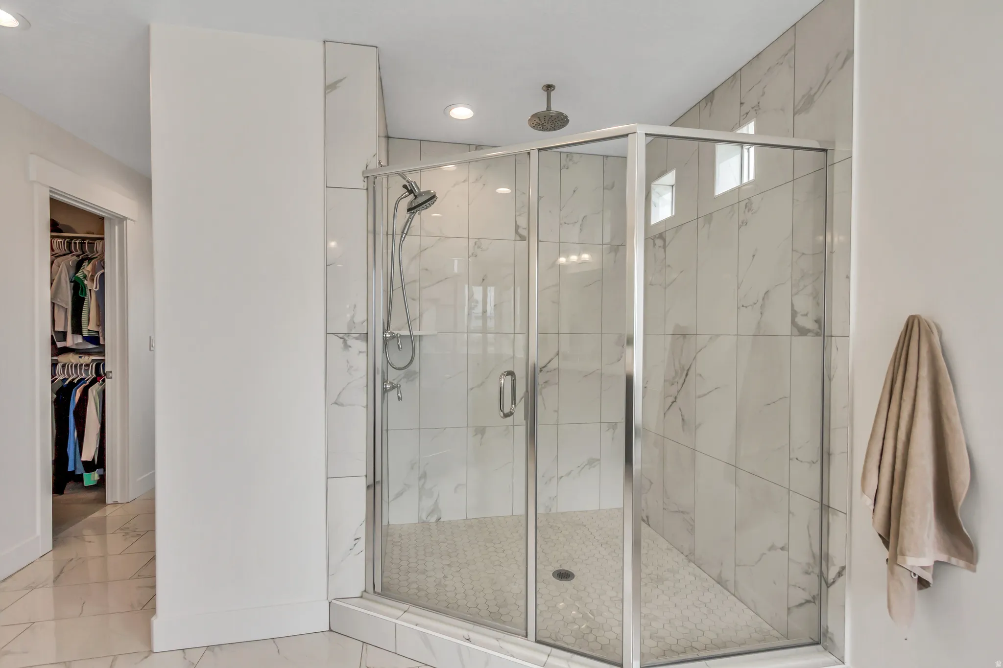 Corner glass-enclosed shower with rain shower head, white marble-look wall tiles and a hexagonal tile floor