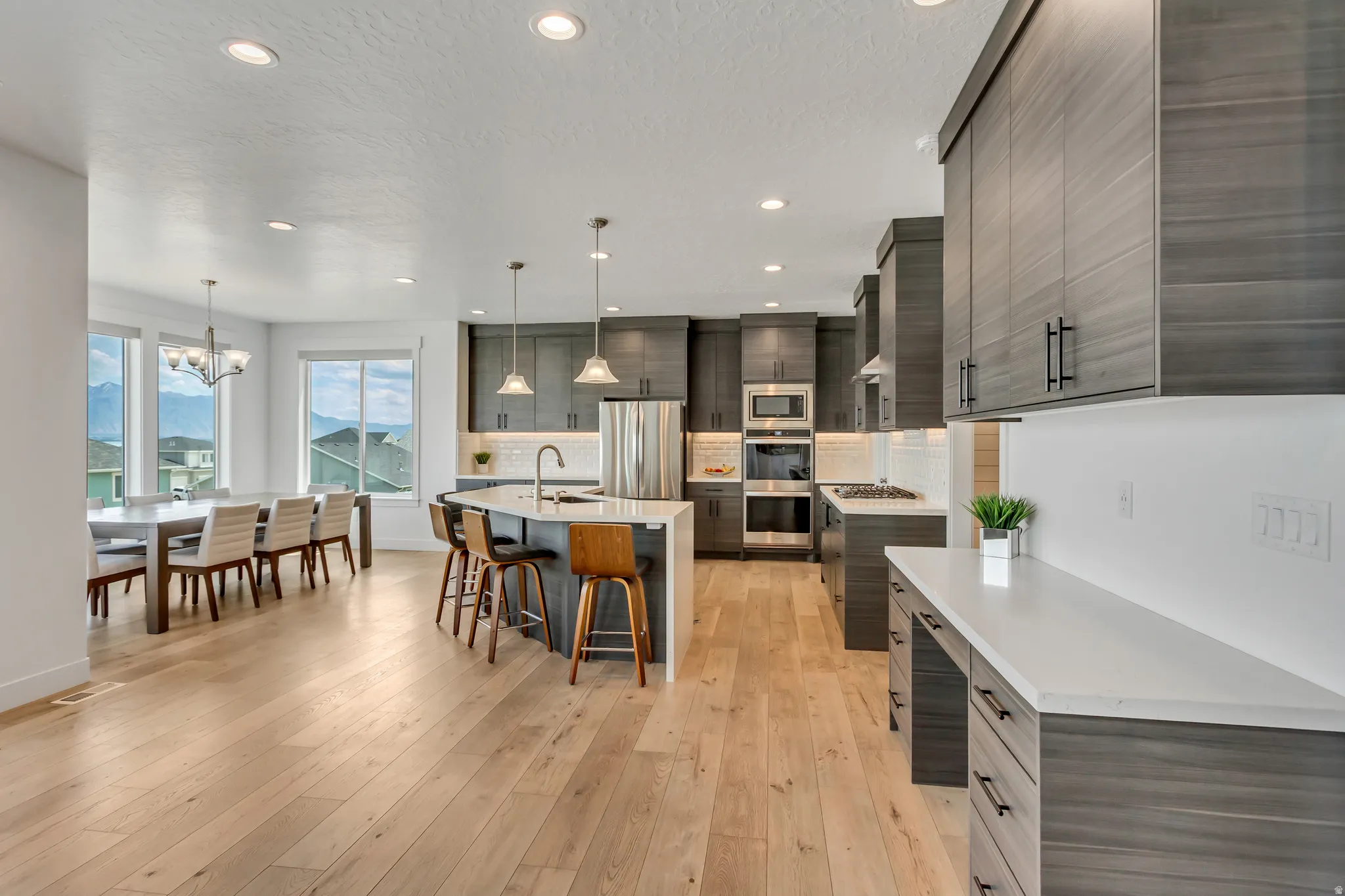 Kitchen and dining area featuring light wood-finish flooring, waterfall quartz island, double wall ovens and 5 burner gas cooktop.