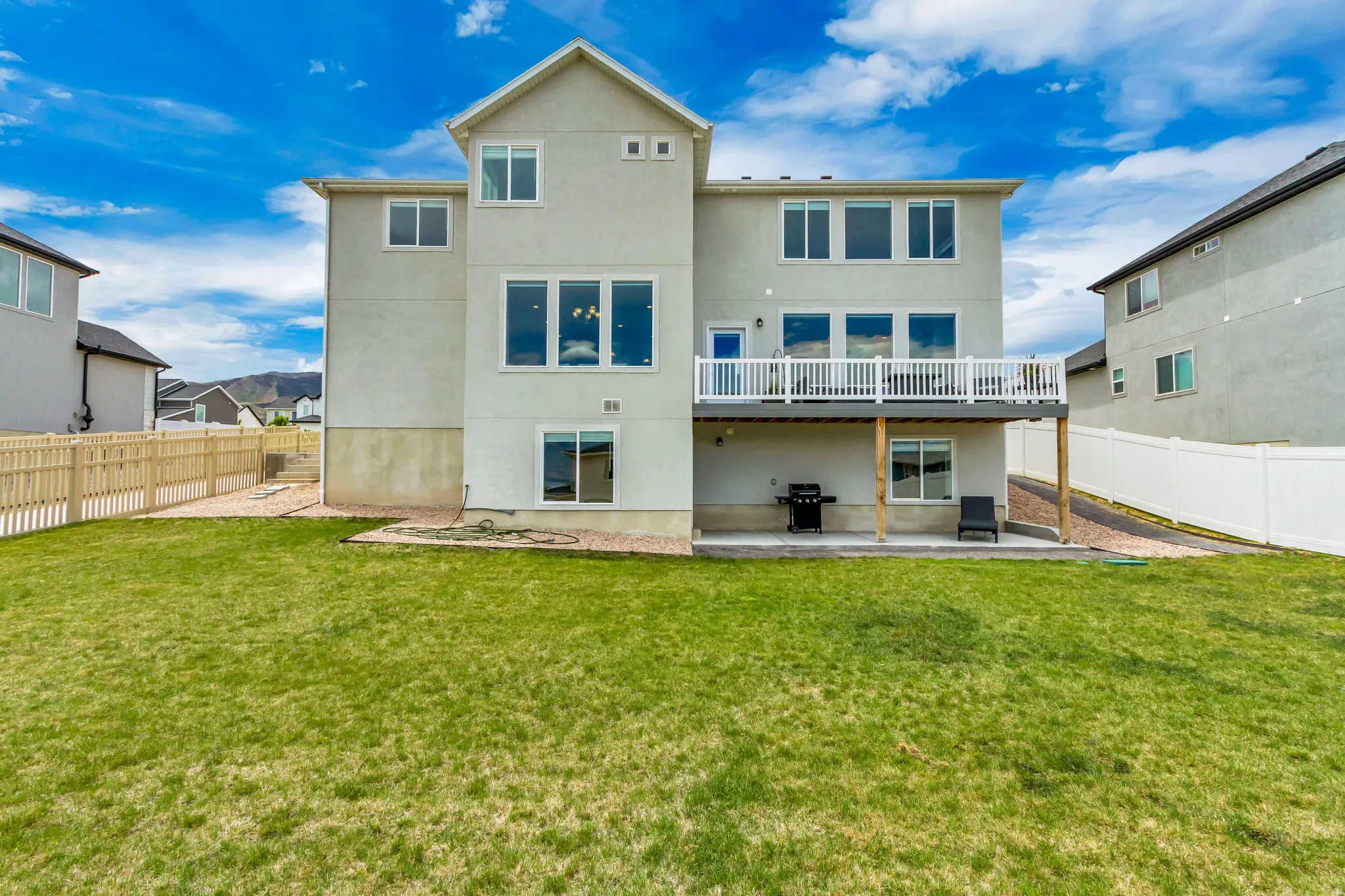 Expansive rear elevation featuring a multi-level design, an upper-level deck with white railings, and a ground-level patio