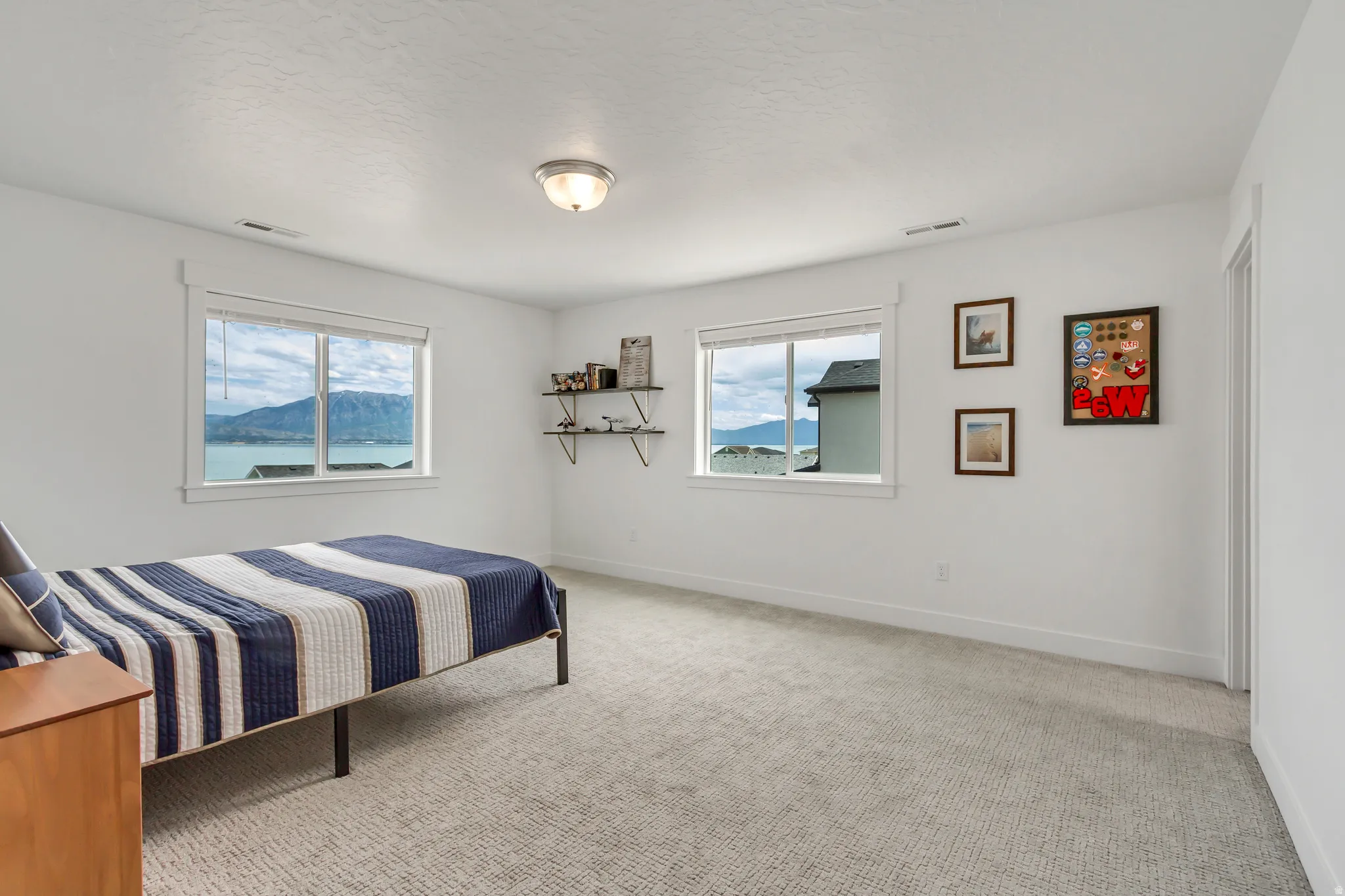 Fourth bedroom upstairs featuring two large windows, neutral carpeting, and wall-mounted shelving