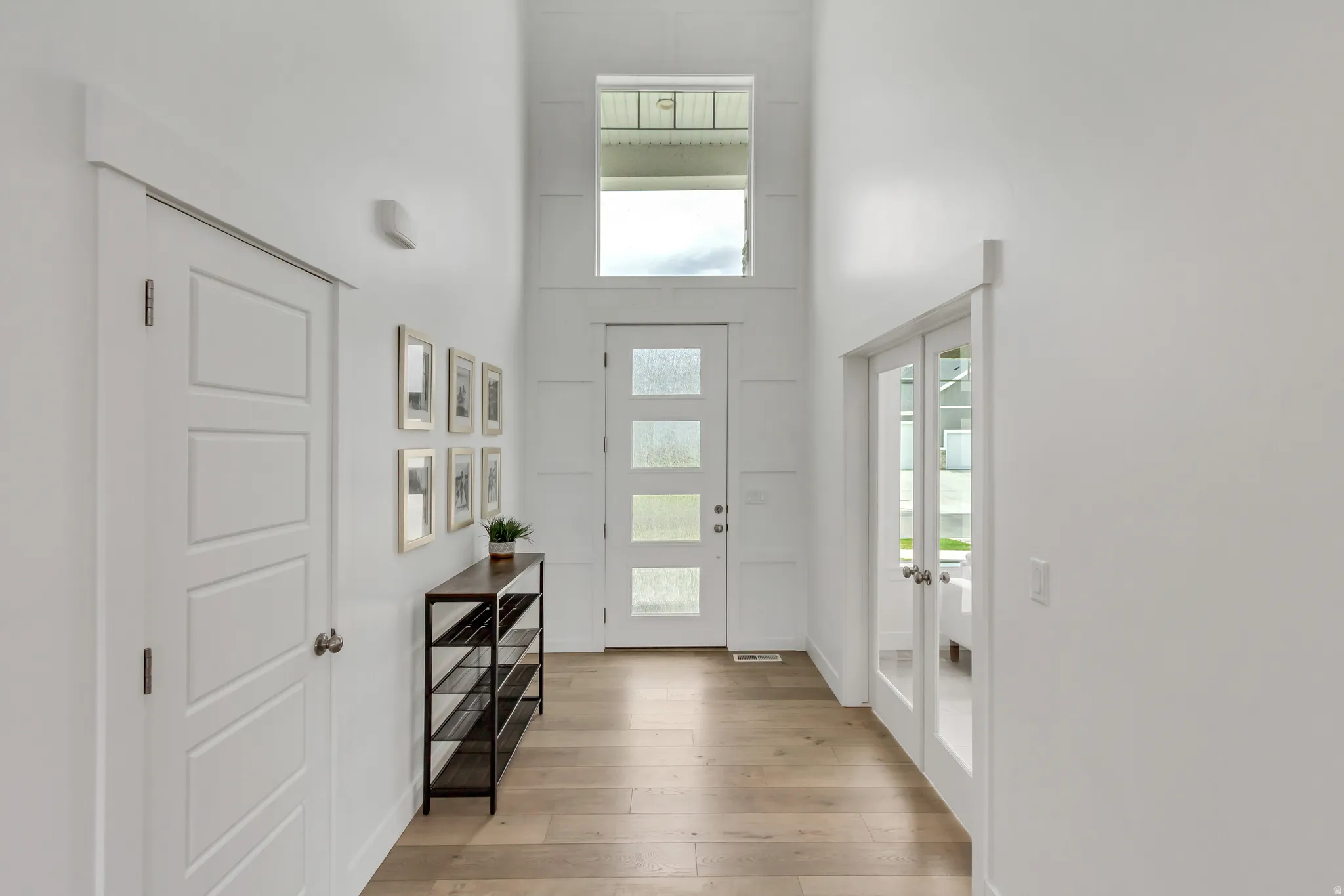 Foyer featuring light wood-finish flooring, a contemporary entry door with frosted glass panels, a transom window, and white panel doors