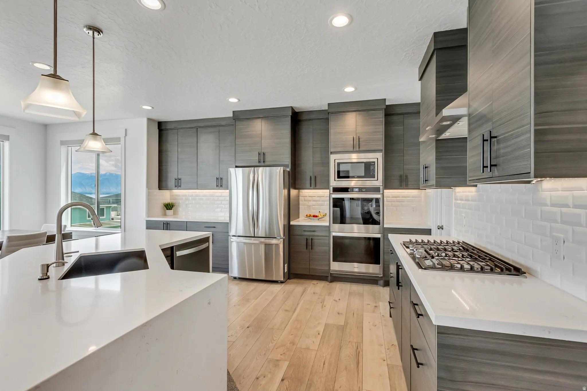 Modern kitchen featuring a large island with an undermount sink and gooseneck faucet, double wall ovens and 5 burner gas cooktop.