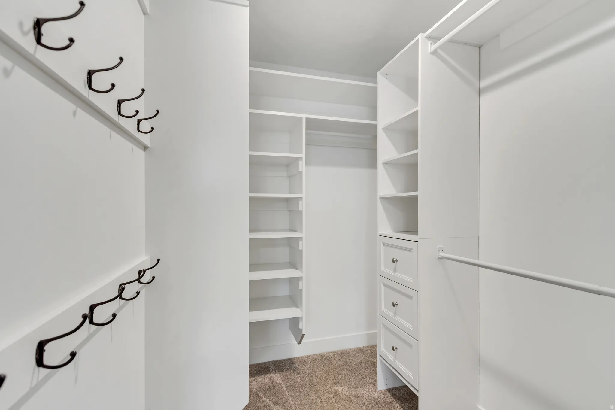 Basement bedroom includes custom closet system featuring multiple hanging rods, integrated shelving units, three pull-out drawers, and wall-mounted coat hooks.