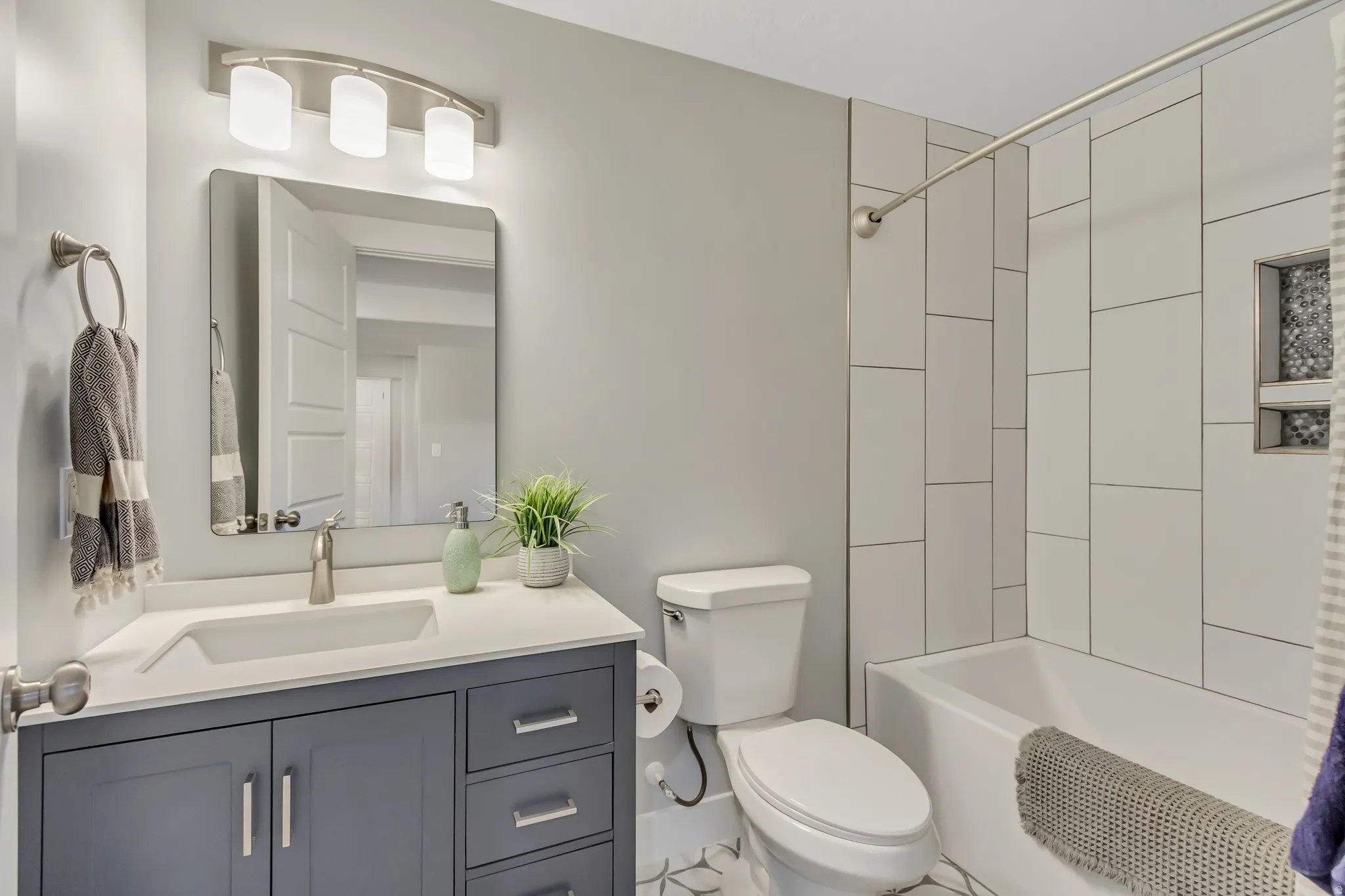 Basement full bathroom featuring shower tile surround to ceiling, a tile floor, dark gray vanity with a white countertop, an undermount sink, and a brushed nickel faucet