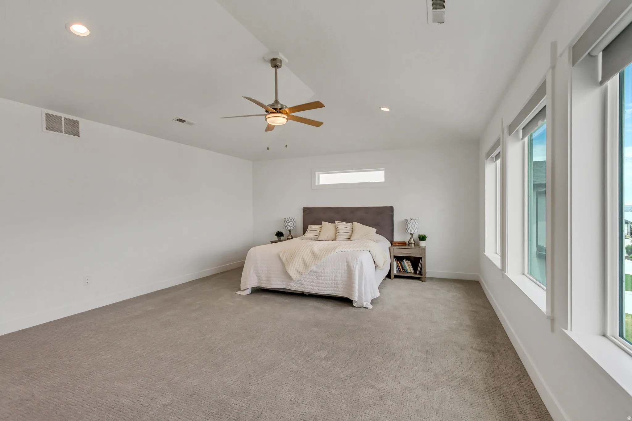 Large primary bedroom featuring neutral carpeting, recessed ceiling lighting, a ceiling fan with light fixture, and multiple large windows providing ample natural light