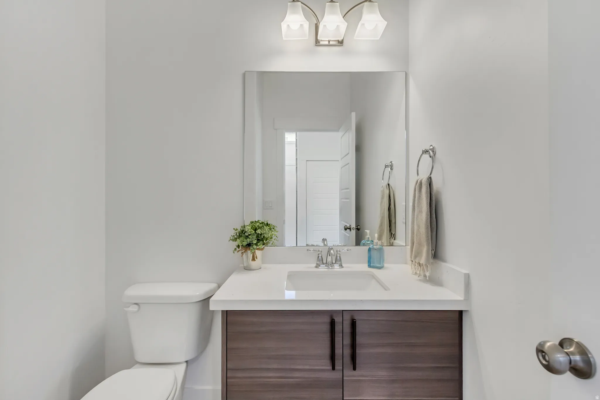 Main floor half bath featuring dark wood-finish vanity with black hardware, white countertop, integrated sink, and an overhead light fixture with three sconces