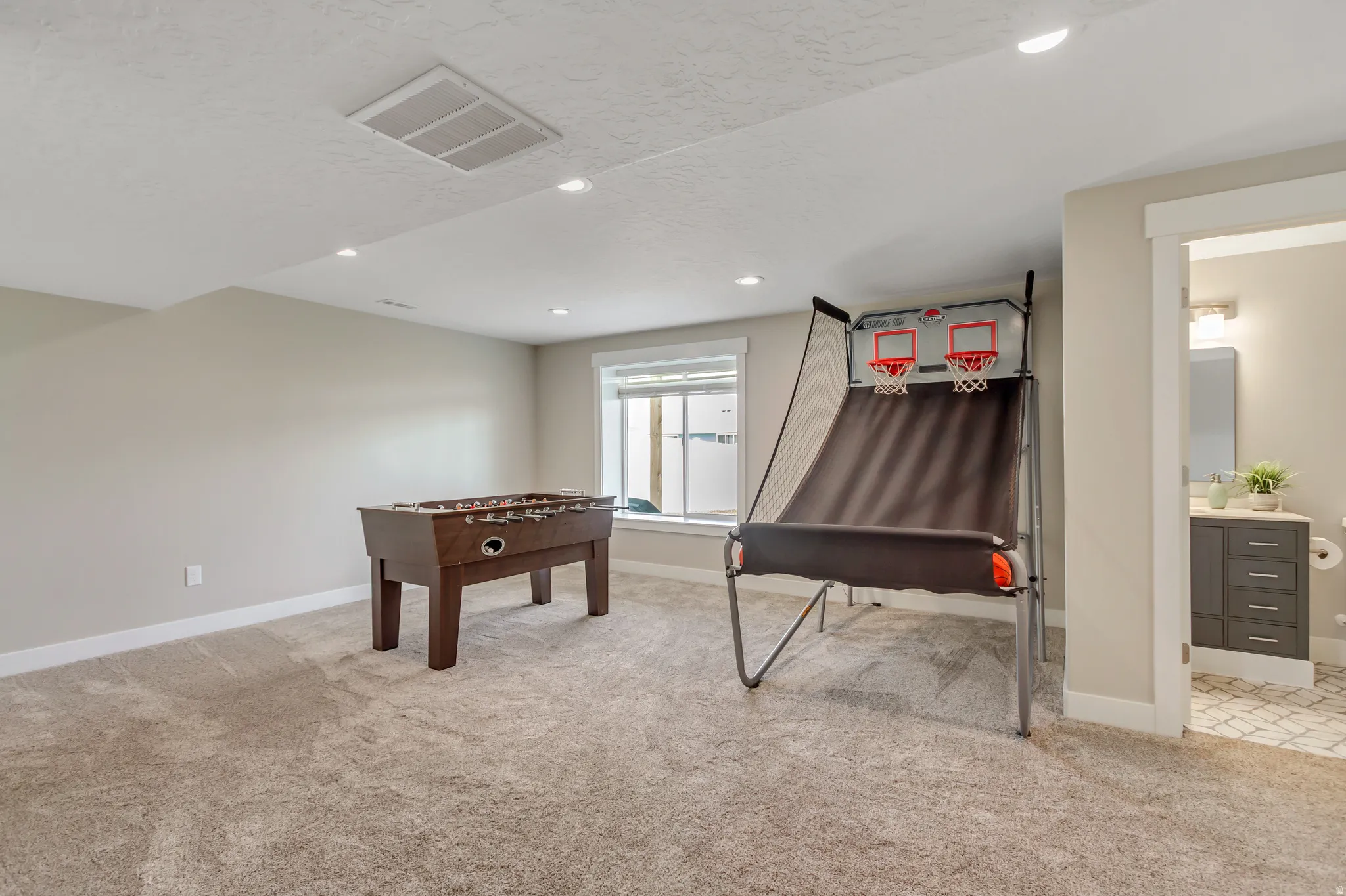 Spacious recreation room featuring neutral carpeting, recessed lighting, and window