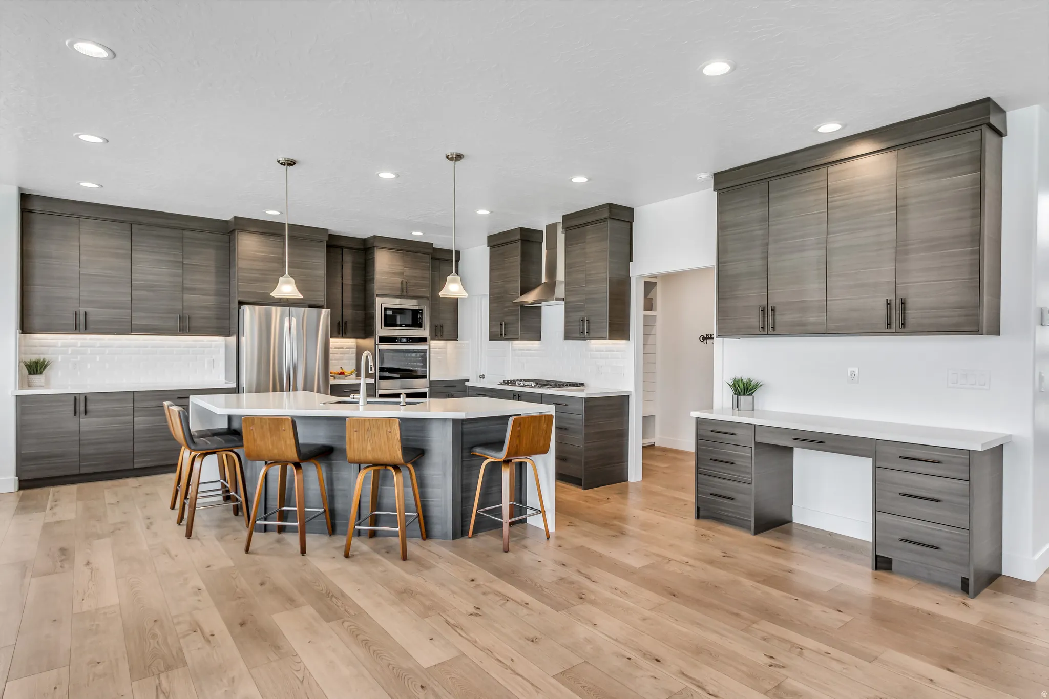 Open-concept kitchen featuring wood-finish flooring, a large central island with seating, stainless steel appliances and hood, extensive cabinetry, and recessed lighting