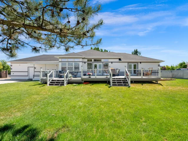 Expansive rear lawn with a full-width deck featuring dual staircases and white railings
