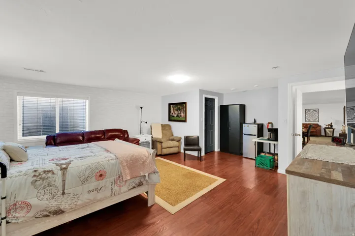 Spacious room featuring wood-finish flooring, a large egress window with blinds, and white painted brick wall accents