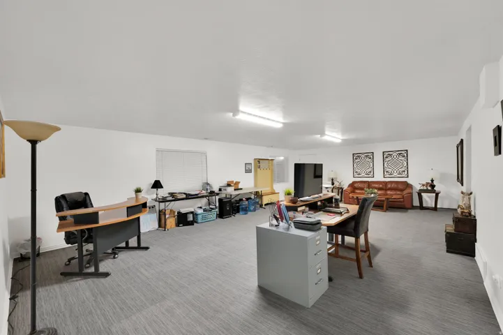 Expansive open-concept space featuring light gray carpet flooring, white walls, multiple windows, and overhead fluorescent lighting