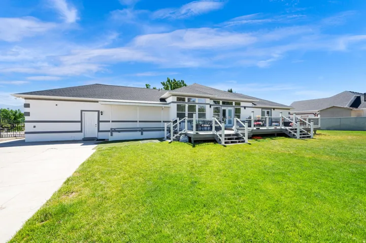 Rear exterior featuring a walkout basement, expansive lawn, a multi-level deck, multiple sets of glass panel double doors, and a covered patio area