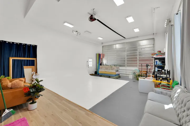 Photo Studio - Spacious studio with a white cyc wall, light wood-finish flooring, and a large translucent panel overhead door