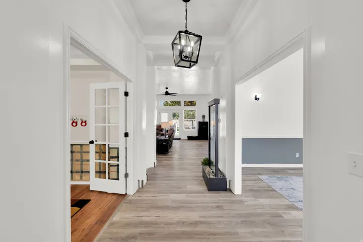 Hallway featuring wood-finish flooring, recessed lighting, crown molding, a modern chandelier, and a black planter with greenery