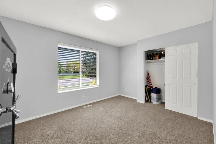 Carpeted room featuring light gray walls, a window with horizontal blinds, a white trim baseboard, and a white six-panel bi-fold closet door