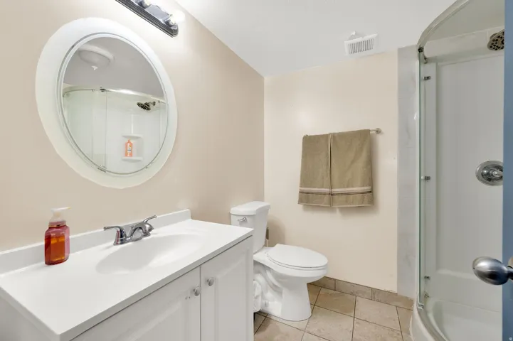 Bathroom featuring a white vanity with integrated sink, chrome faucet, oval wall mirror, and a shower with a curved glass enclosure