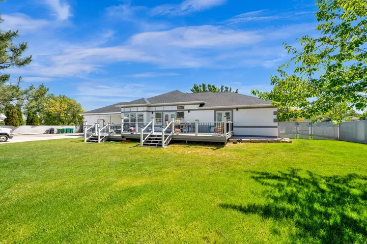 Expansive backyard featuring a manicured lawn, multi-level deck with glass panel railings, and multiple access points from the home