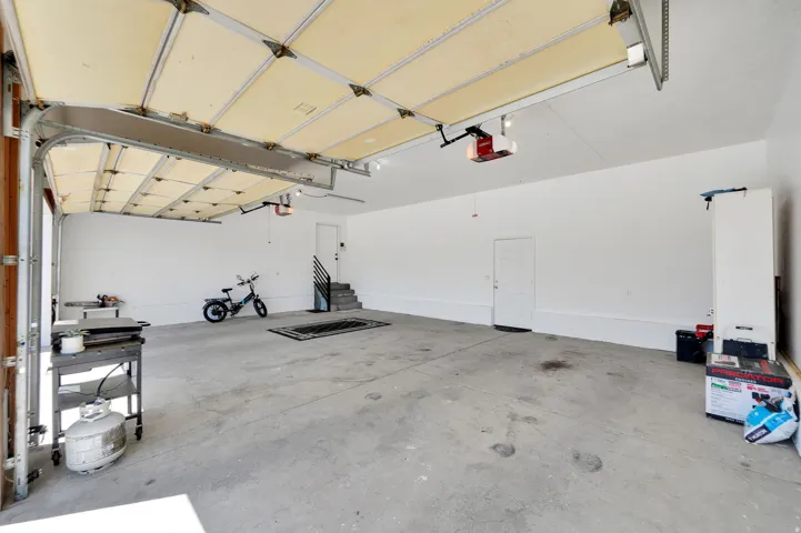 Spacious garage featuring a concrete floor, white walls, an overhead garage door, and a dedicated entry door