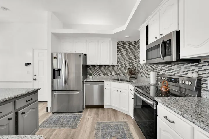 Kitchen featuring white cabinetry and gray lower island cabinetry, stainless steel appliances, granite countertops, and a mosaic tile backsplash