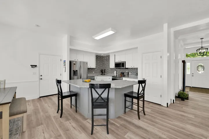 Kitchen featuring a large light gray island with seating, stainless steel appliances, white cabinetry, and a mosaic tile backsplash