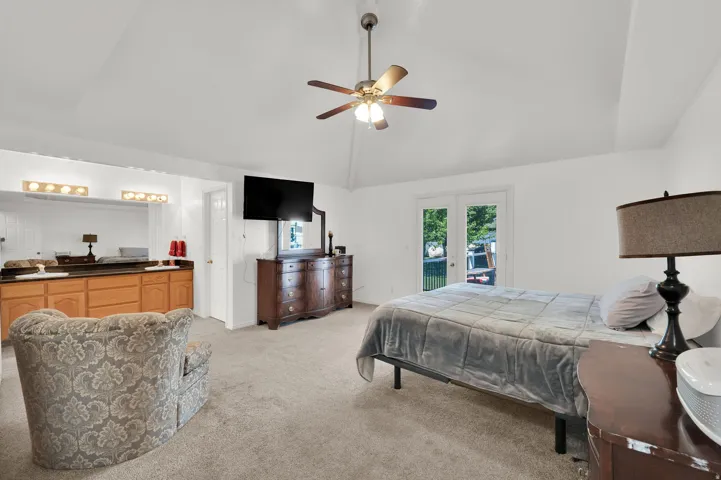 Vaulted ceiling with ceiling fan, French doors to exterior, wood-finish cabinetry, vanity lighting, and wall-mounted television