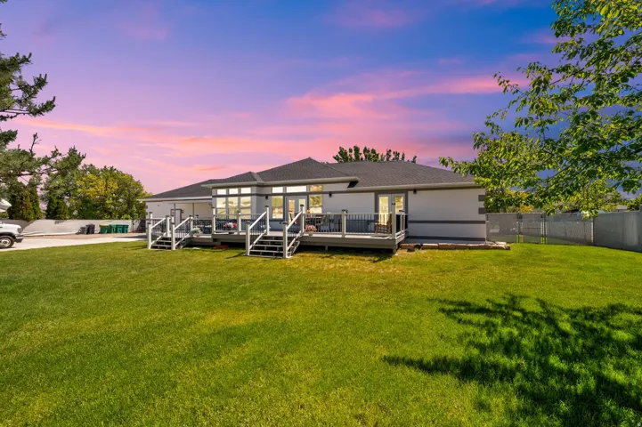 Expansive rear lawn featuring a contemporary gray deck with glass panel railings and multiple access points