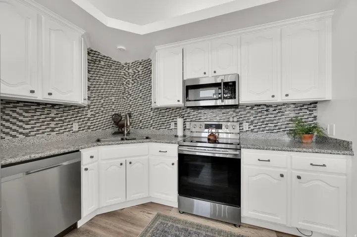 Kitchen featuring white cabinetry, gray speckled countertops, a mosaic tile backsplash, and stainless steel appliances including a microwave, range, and dishwasher