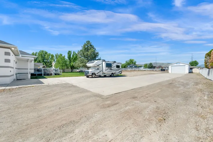 Expansive gravel lot featuring a concrete parking pad, a white detached garage with a roll-up door, and a retaining wall