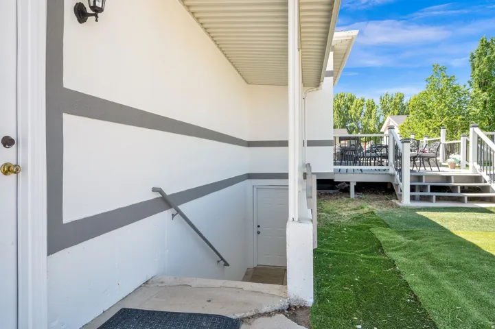 Exterior features a white and grey painted stucco wall, a lower level entry door, and a handrail descending to a concrete pad