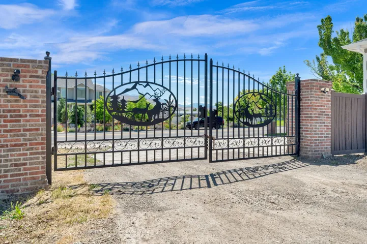 Wrought iron entry gate featuring decorative deer and mountain cutouts, brick pillars, and a gravel driveway