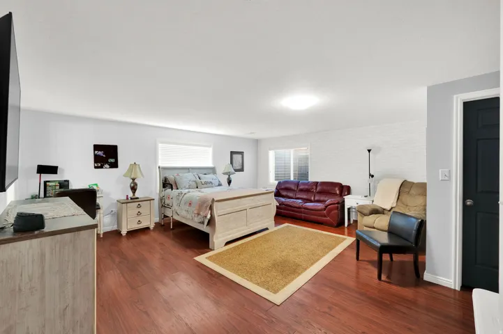 Spacious room featuring rich wood-finish flooring, white walls, and a recessed window with blinds