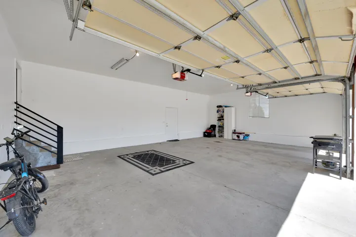Spacious garage featuring a concrete floor, overhead garage door with automatic opener, and a staircase with a black metal railing